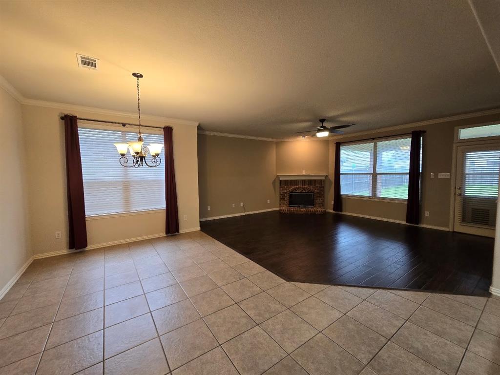 213 Willet Court Little Elm, TX 75068 - Photo 7 of 28 Unfurnished living room with ornamental molding, a ceiling fan, light tile patterned flooring, hanging lights, and a brick fireplace