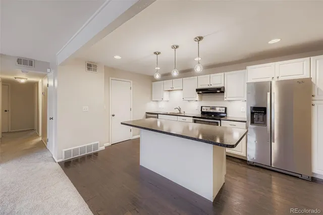 a kitchen with granite countertop a refrigerator a sink dishwasher a stove and white cabinets with wooden floor