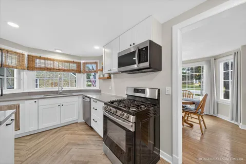 a kitchen with stainless steel appliances granite countertop a stove top oven a sink dishwasher a dining table and chairs with wooden floor