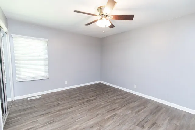 an empty room with wooden floor fan and windows