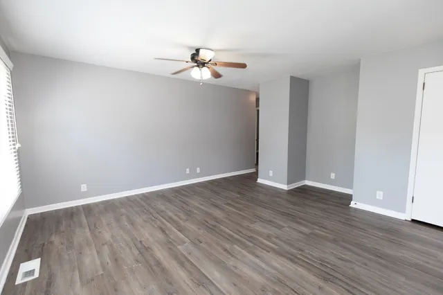 an empty room with wooden floor fan and windows