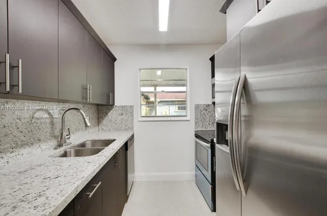 a kitchen with stainless steel appliances granite countertop a refrigerator a sink a stove and a refrigerator with wooden floor