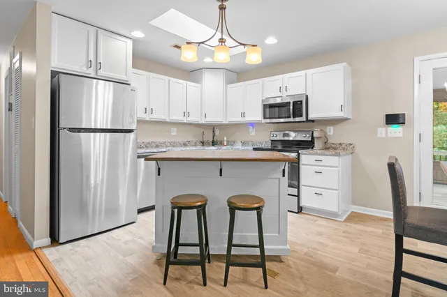 a kitchen with stainless steel appliances granite countertop a refrigerator a stove a sink dishwasher and white cabinets with wooden floor