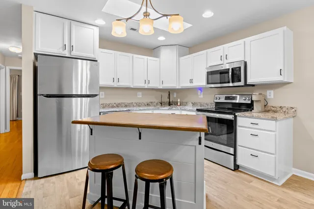 a kitchen with stainless steel appliances granite countertop a refrigerator a sink dishwasher a stove and white cabinets with wooden floor