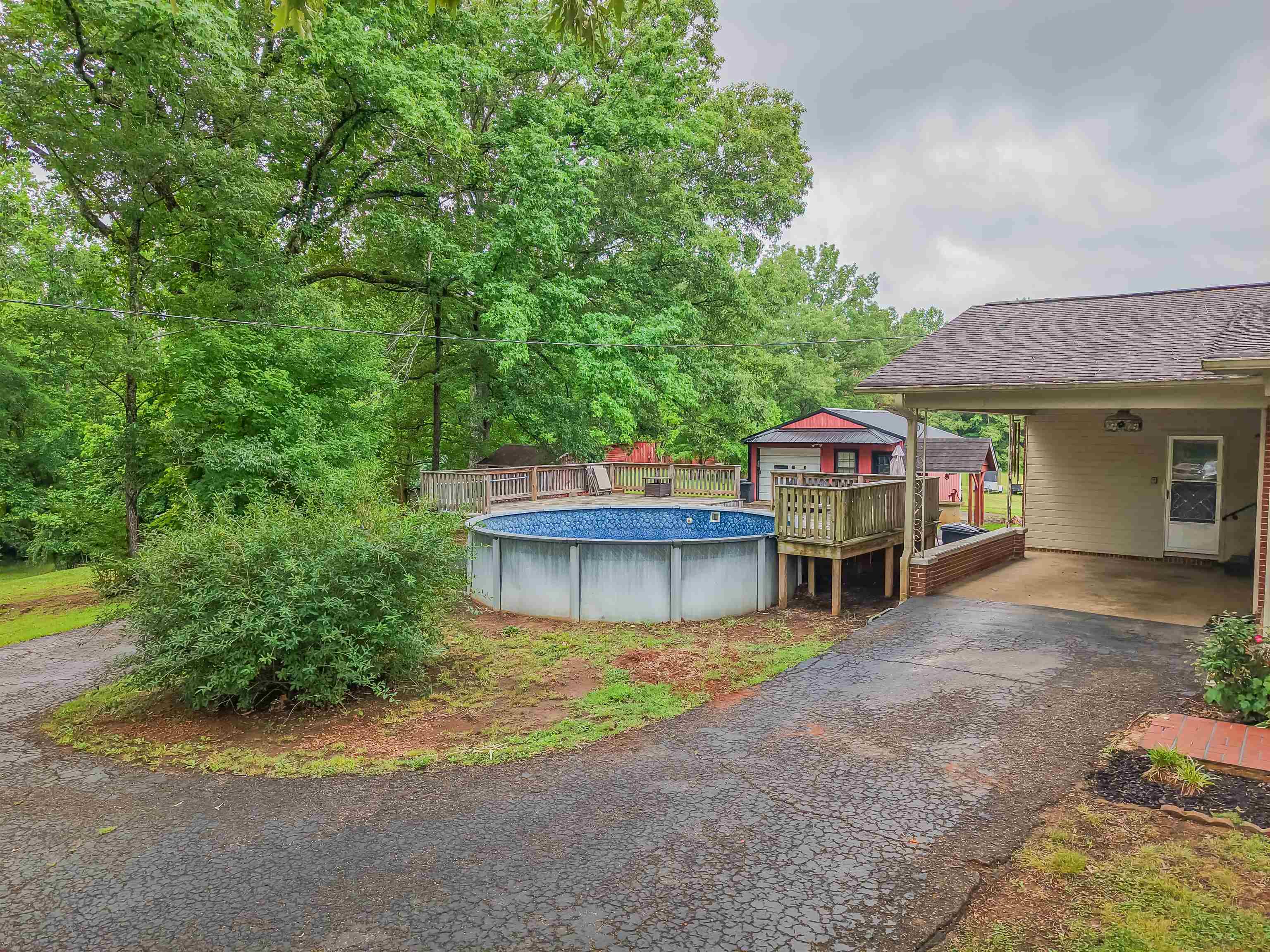 336 57th Highway West Ramer, TN 38367 - Photo 23 of 39 Backyard featuring an above-ground pool with a surrounding wooden deck, a paved driveway, and a covered carport with an exterior light fixture