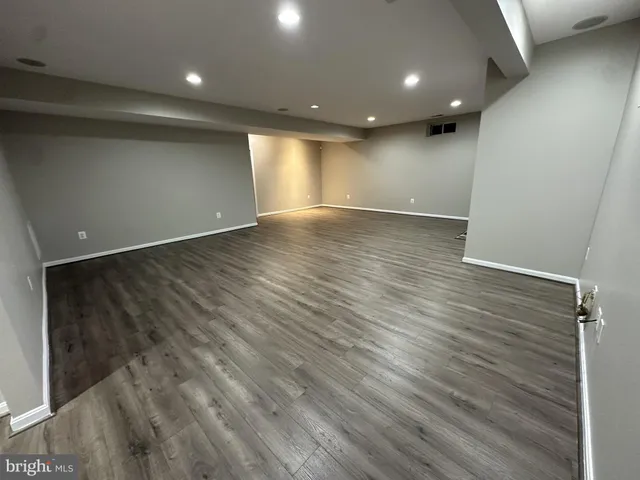a view of an empty room with wooden floor and fan