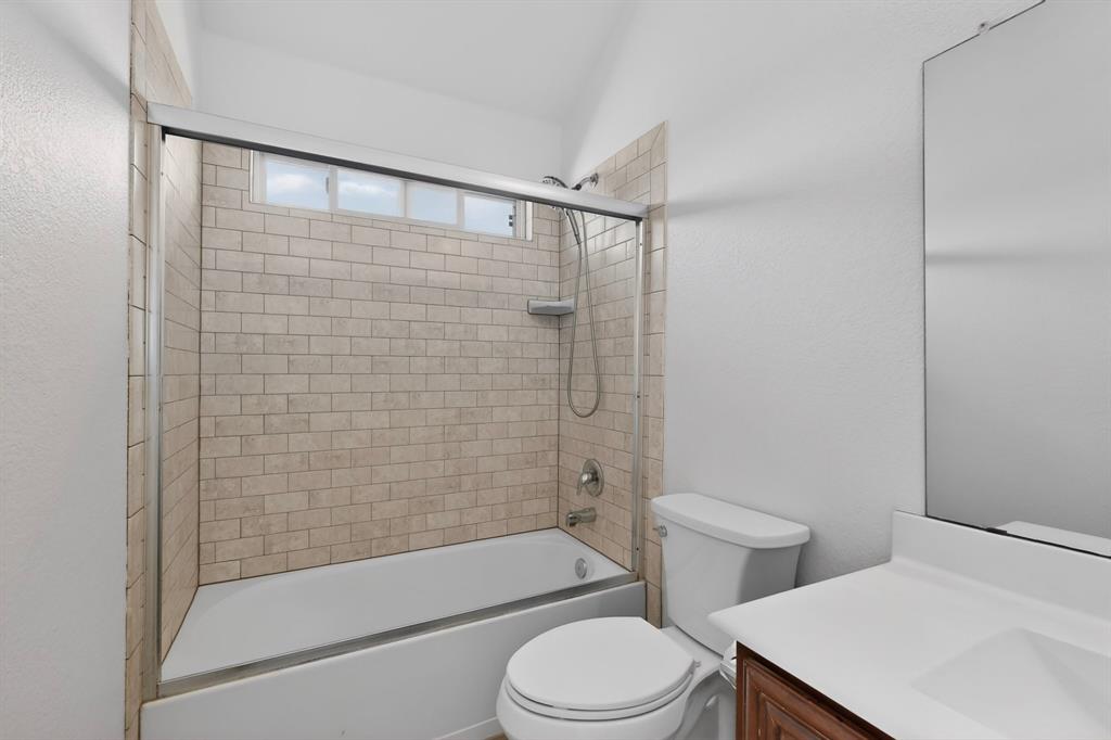 426 Harding Lane Lavon, TX 75166 - Photo 38 of 40 Bathroom featuring a tiled shower surround, bathtub with sliding glass enclosure, white toilet, and a vanity with a white countertop and integrated sink