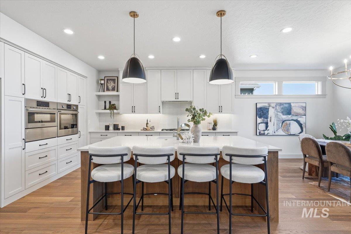 6762 South Messner Way Meridian, ID 83642 - Photo 6 of 35 Gourmet kitchen featuring white shaker cabinetry, stainless steel double ovens, a large center island with a light-toned countertop, and wood-finish flooring