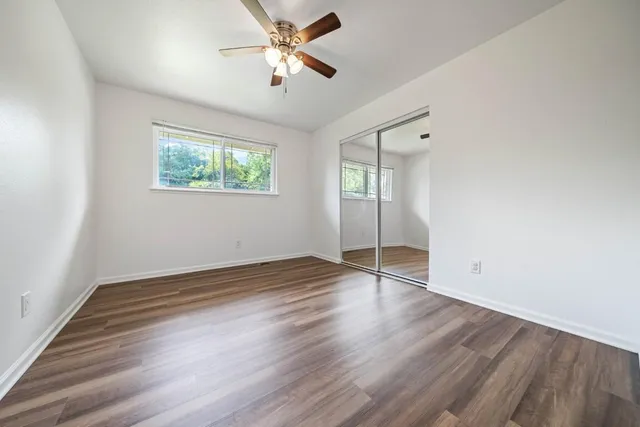 an empty room with wooden floor chandelier fan and windows
