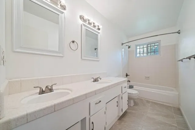 a bathroom with a double vanity sink a toilet and a bathtub