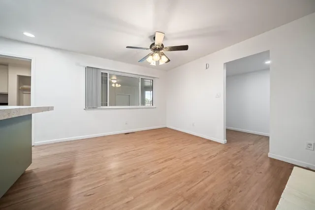 an empty room with wooden floor ceiling fan and windows
