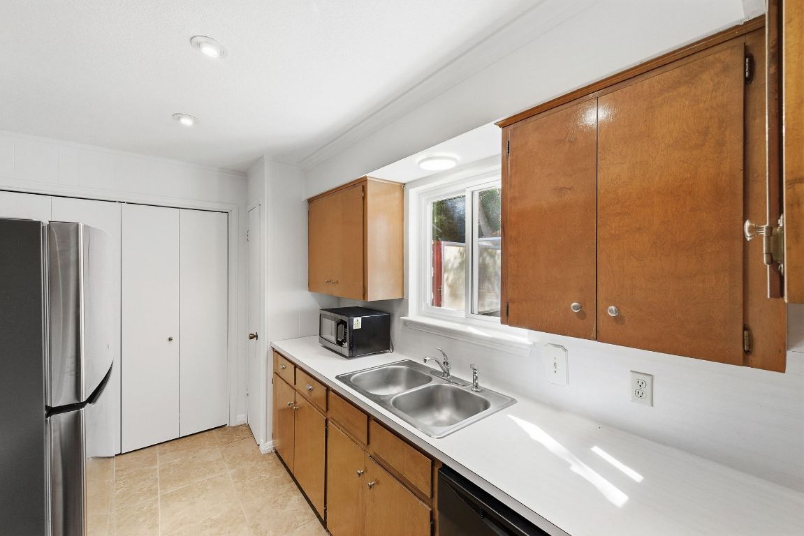 6210 Shadow Valley Drive, Unit B Austin, TX 78731 - Photo 11 of 28 Kitchen with freestanding refrigerator, light countertops, brown cabinetry, black microwave, and dishwasher