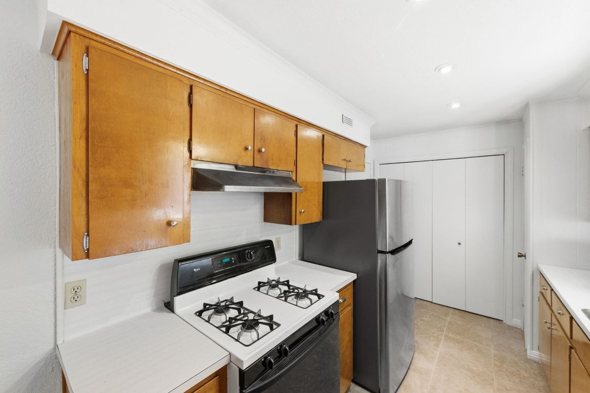 6210 Shadow Valley Drive, Unit B Austin, TX 78731 - Photo 12 of 28 Kitchen with white range with gas cooktop, light countertops, brown cabinetry, freestanding refrigerator, and under cabinet range hood