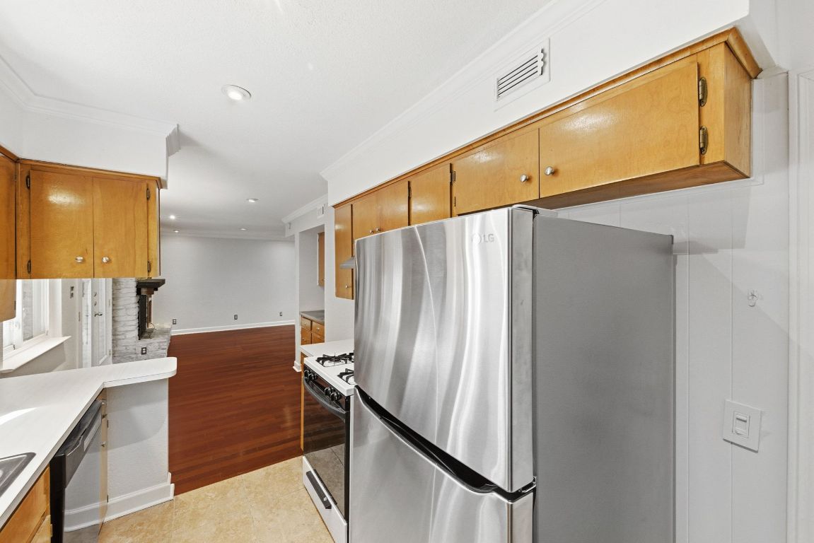 6210 Shadow Valley Drive, Unit B Austin, TX 78731 - Photo 14 of 28 Kitchen featuring stainless steel appliances, crown molding, light tile patterned floors, light countertops, and brown cabinetry