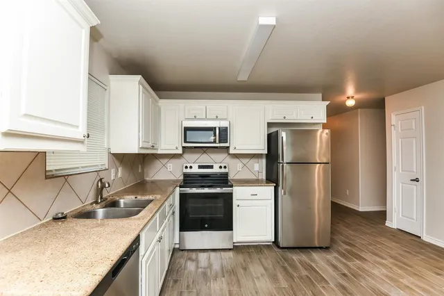 a kitchen with stainless steel appliances granite countertop a stove a sink dishwasher a refrigerator and white cabinets with wooden floor