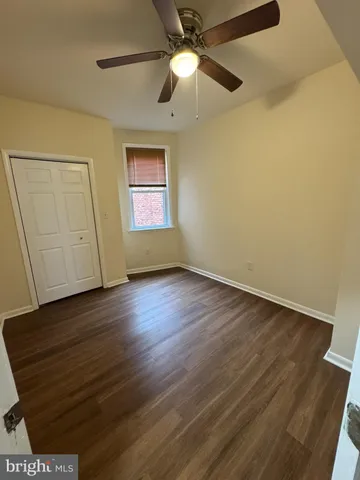 a view of an empty room with wooden floor and a ceiling fan