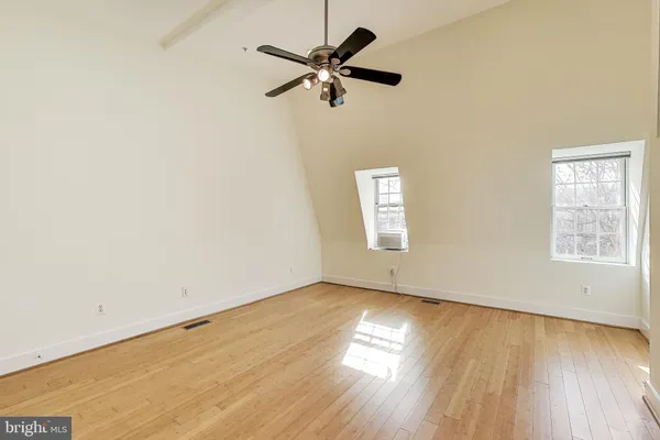 an empty room with wooden floor fan and windows