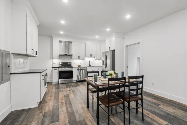 a kitchen with kitchen island granite countertop wooden floors white cabinets and appliances