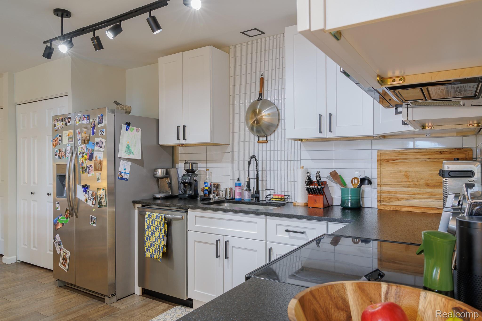 1989 Klingensmith Road, Unit 46 Bloomfield Hills, MI 48302 - Photo 23 of 41 Modern kitchen featuring white shaker cabinetry, black countertops, stainless steel appliances, a white subway tile backsplash, and wood-finish flooring