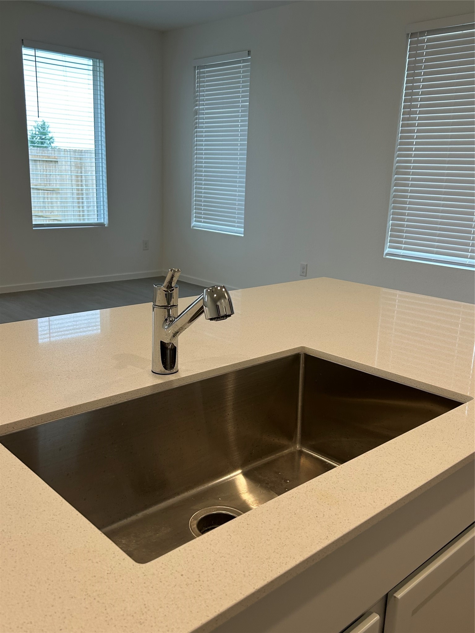 26419 Virginia Wild Rye Lane Katy, TX 77493 - Photo 13 of 31 This photo showcases a modern kitchen island with a sleek stainless steel sink and a polished chrome faucet. The space is bright and airy, featuring large windows with blinds, providing ample natural light and a view of a fenced backyard.