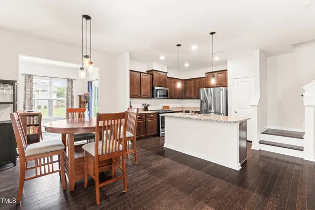 a kitchen with stainless steel appliances granite countertop a refrigerator a stove top oven a sink dishwasher a dining table and chairs with wooden floor