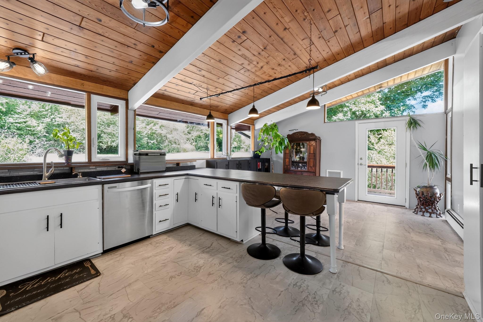424 Laroe Road Chester, NY 10918 - Photo 32 of 43 Kitchen featuring a vaulted wood-paneled ceiling, white cabinetry with black hardware, dark countertops, a stainless steel dishwasher, and large windows