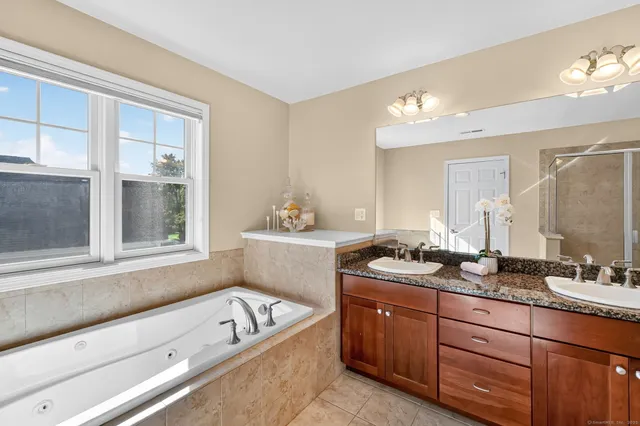 a bathroom with a granite countertop tub a double vanity sink a window and a mirror