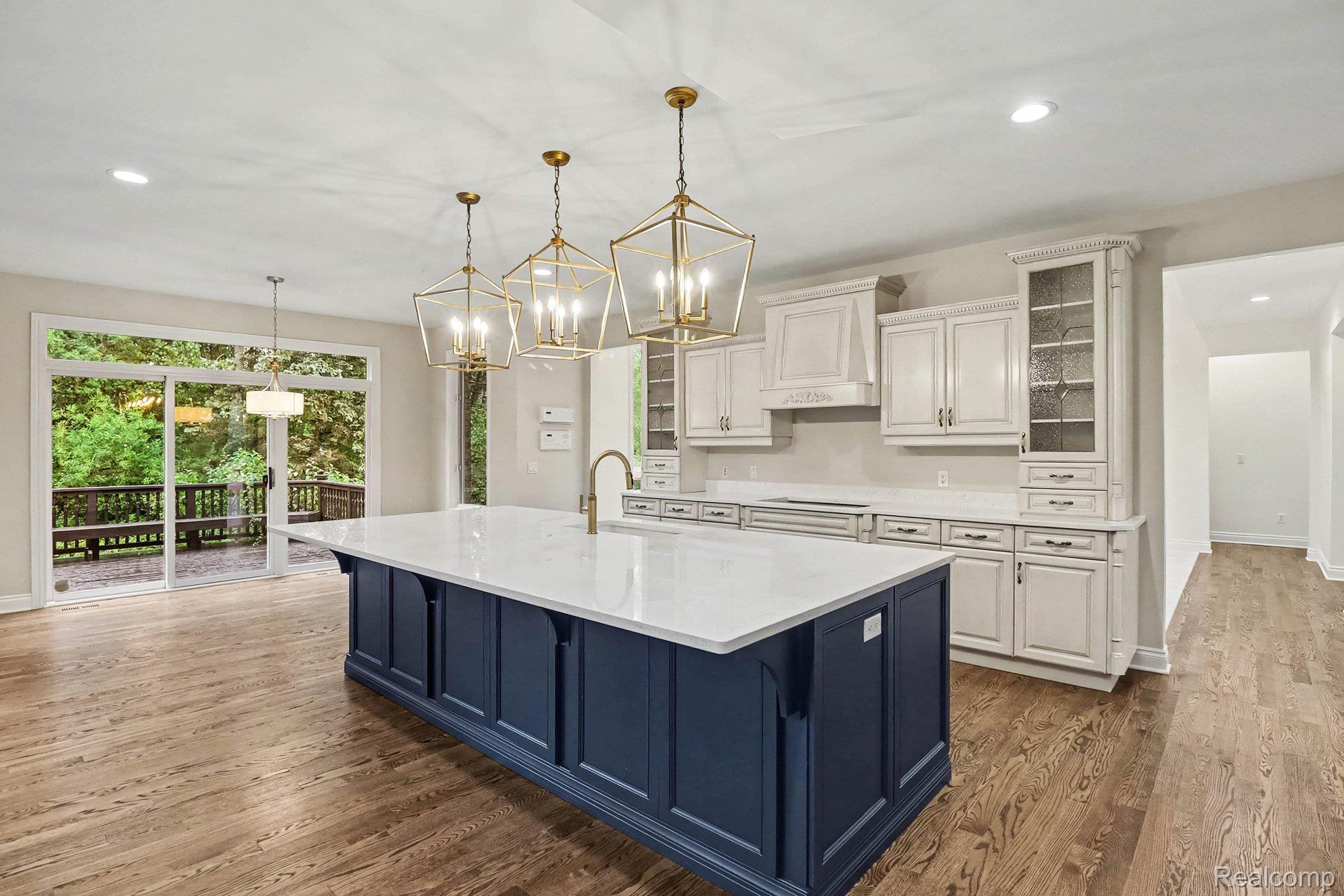 4875 Green Meadow Lane Rochester, MI 48306 - Photo 20 of 60 Kitchen featuring a large central island with a white countertop, white cabinetry with display glass, stainless-steel appliances, and wood-finish flooring
