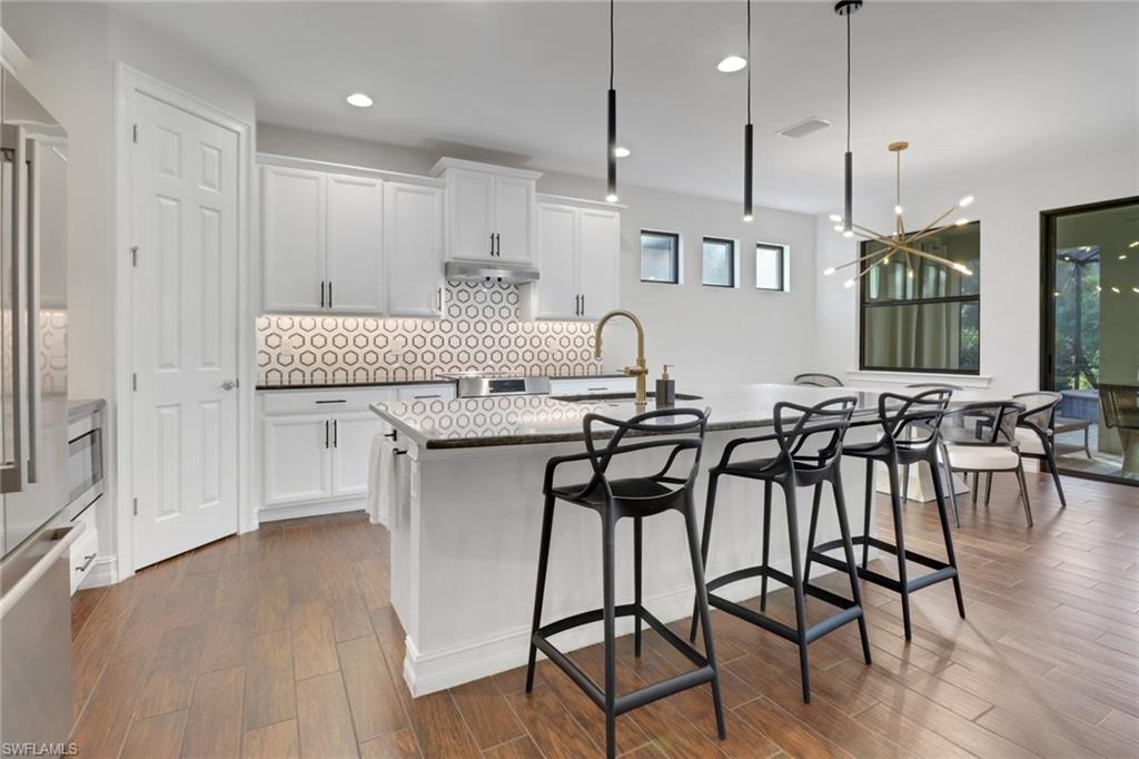 14374 Tuscany Pointe Trail Naples, FL 34120 - Photo 11 of 38 an open kitchen with granite countertop a stove a table and chairs with wooden floor