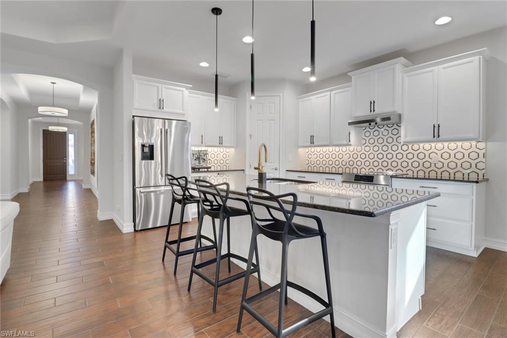 14374 Tuscany Pointe Trail Naples, FL 34120 - Photo 12 of 38 a kitchen with stainless steel appliances granite countertop a stove top oven a refrigerator a sink and white cabinets with wooden floor