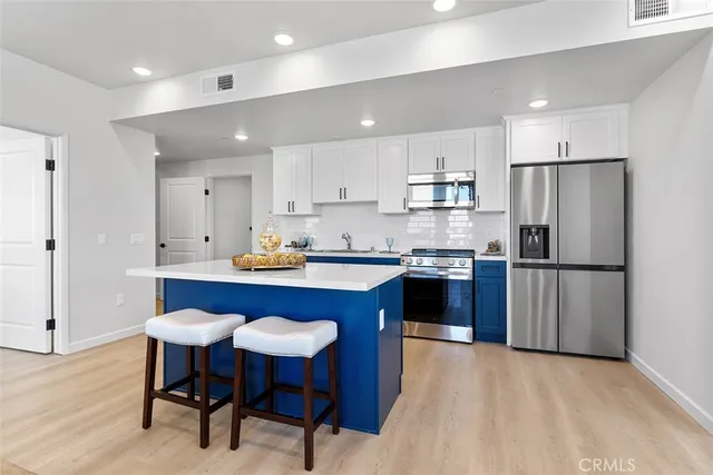 a kitchen with stainless steel appliances granite countertop a refrigerator a sink dishwasher a stove and white countertops with wooden floor