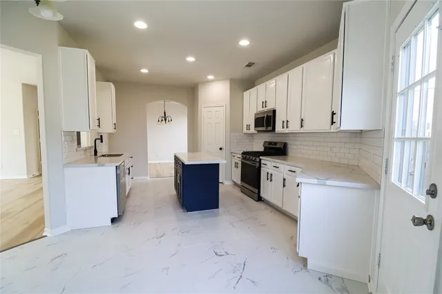 a large kitchen with stainless steel appliances granite countertop a stove a sink a refrigerator and white cabinets