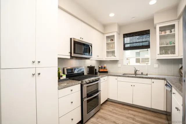 a kitchen with stainless steel appliances granite countertop white cabinets a sink a stove a window and a microwave