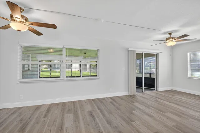 an empty room with wooden floor fan and windows