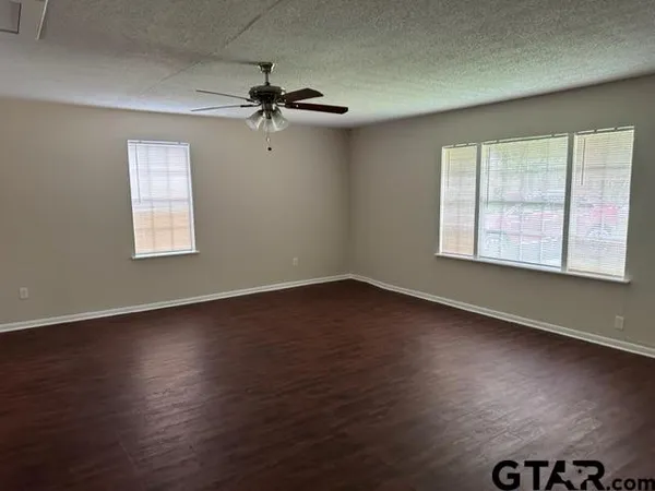 an empty room with wooden floor chandelier fan and windows