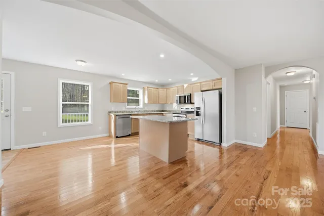 a view of kitchen with stainless steel appliances granite countertop a refrigerator a stove top oven a sink dishwasher and white cabinets with wooden floor