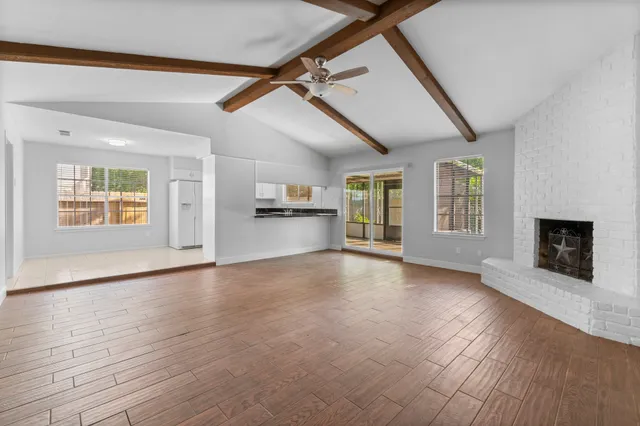 an empty room with wooden floor fireplace and windows