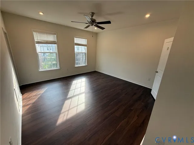 an empty room with wooden floor fan and windows