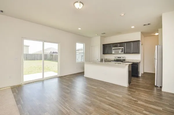 a view of kitchen with granite countertop refrigerator oven sink and white cabinets with wooden floor