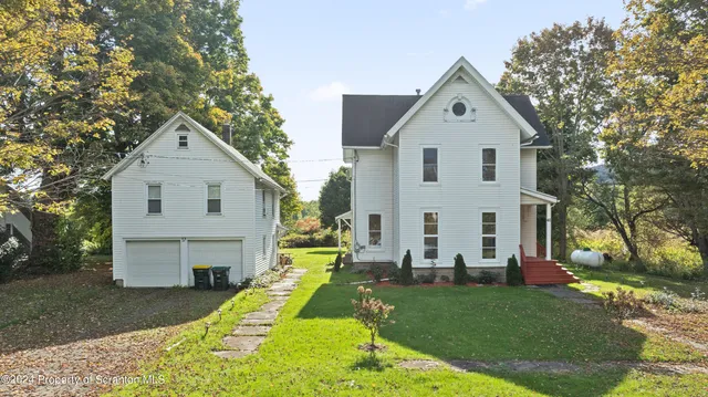 a view of a white house in front of a yard with many windows