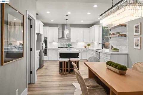 a kitchen with stainless steel appliances kitchen island granite countertop a refrigerator a stove and white cabinets with wooden floor