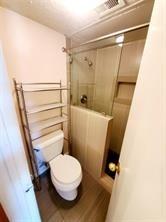 18333 Roehampton Drive, Unit 825 Dallas, TX 75252 - Photo 2 of 7 Bathroom featuring a tiled shower with sliding glass doors, white toilet, and wood-finish flooring