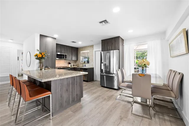 a kitchen with stainless steel appliances kitchen island granite countertop a refrigerator a stove a sink dishwasher and a dining table with wooden floor