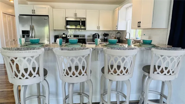 a kitchen with stainless steel appliances kitchen island a table chairs in it and white cabinets