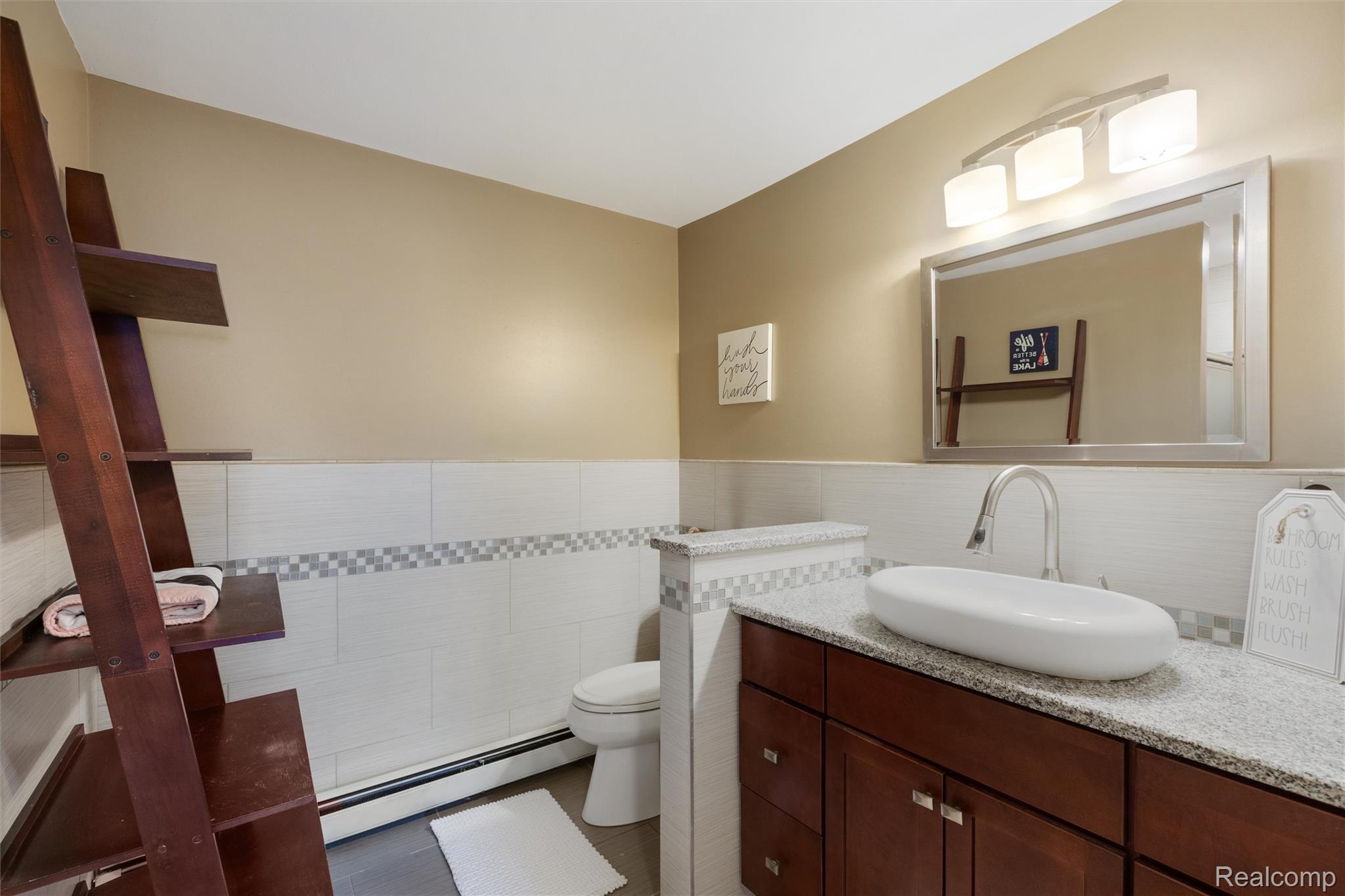 415 Leon Road Walled Lake, MI 48390 - Photo 10 of 47 Bathroom featuring a vessel sink atop a granite-look countertop, dark wood-finish cabinetry, and a full-width mirror with a three-light fixture