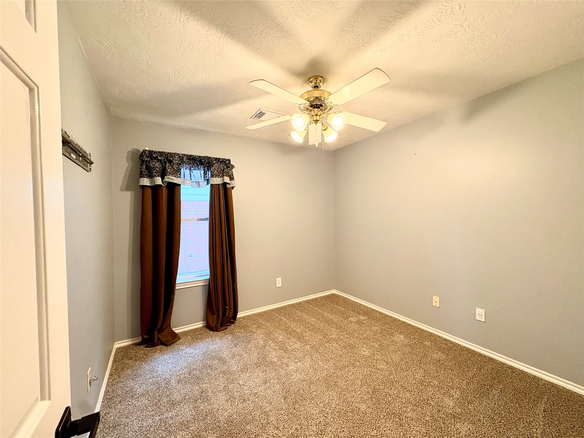 15410 Redbud Berry Way Cypress, TX 77433 - Photo 41 of 49 A cozy, carpeted bedroom with soft gray walls, featuring a ceiling fan with lights. It has a window covered with dark curtains and a decorative valance, providing natural light and a welcoming atmosphere.