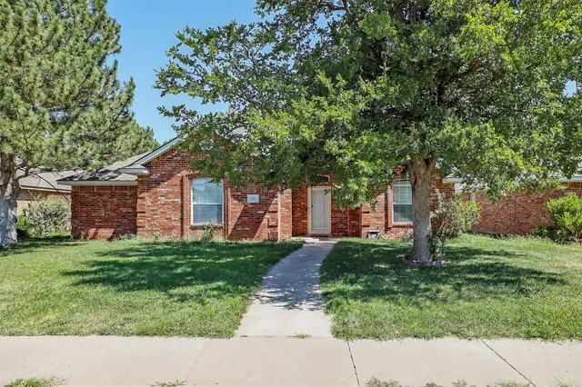 a backyard of a house with plants and large tree