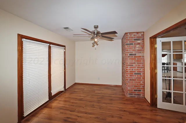 a view of an empty room with wooden floor and a ceiling fan
