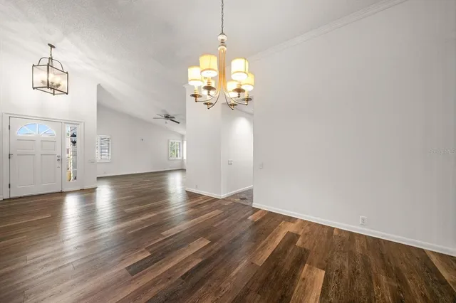 an empty room with wooden floor chandelier and windows