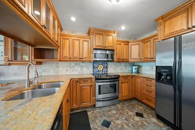 a kitchen with stainless steel appliances granite countertop a sink a stove top oven a refrigerator cabinets and a kitchen island